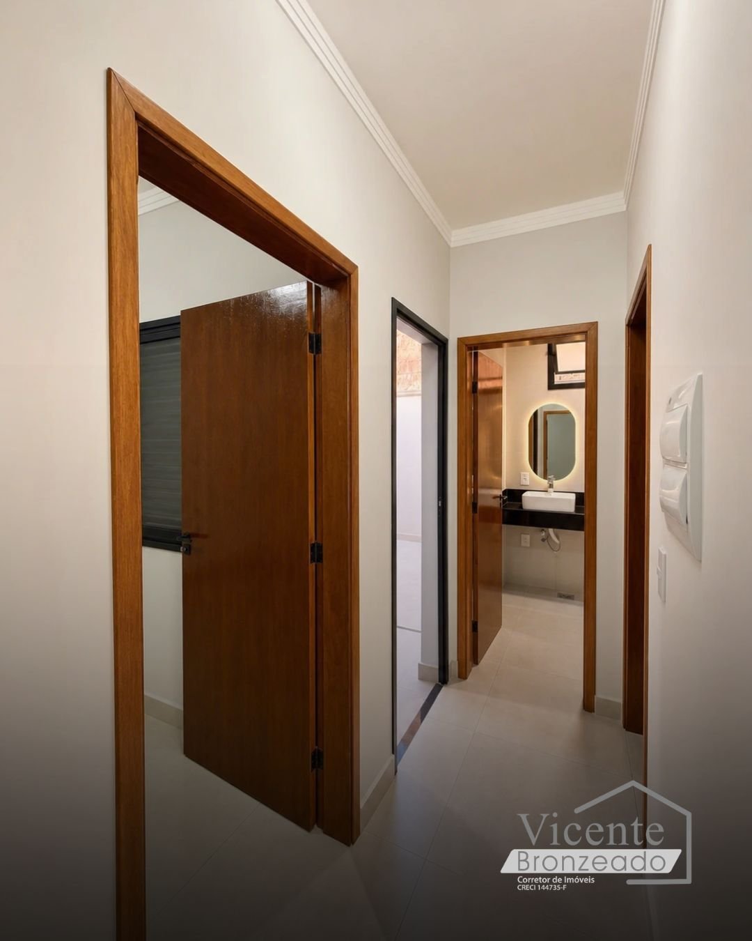 Corredor com portas de madeira e lavabo com espelho iluminado ao fundo
